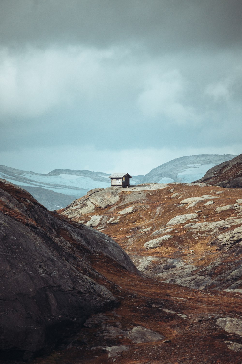 a lone house on a hill with mountains in the background