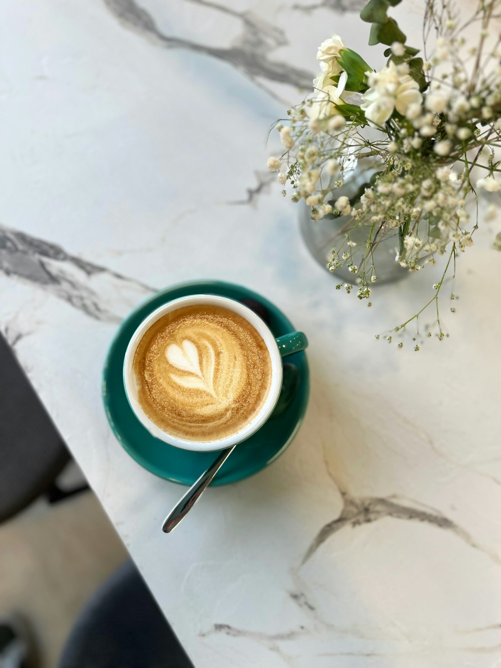 a cup of coffee on a table next to a vase of flowers