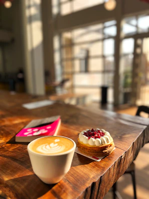 A sunlit café table with a latte, open book, and a Polaroid photo pinned to a corkboard.
