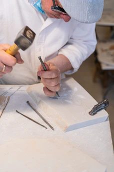Artisan carefully carving a marble vase, surrounded by bright marble pieces in a sunlit workshop