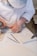 A person wearing a white shirt and a striped cap is carefully carving designs into a stone slab using a chisel and hammer. The workbench is covered in stone dust, and there are additional chisels lying nearby.