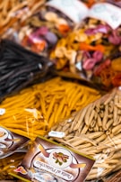Various types of packaged pasta are displayed, featuring a mix of colors and shapes. The packages have clear labels, and the pasta includes traditional as well as colorful varieties made with different ingredients.