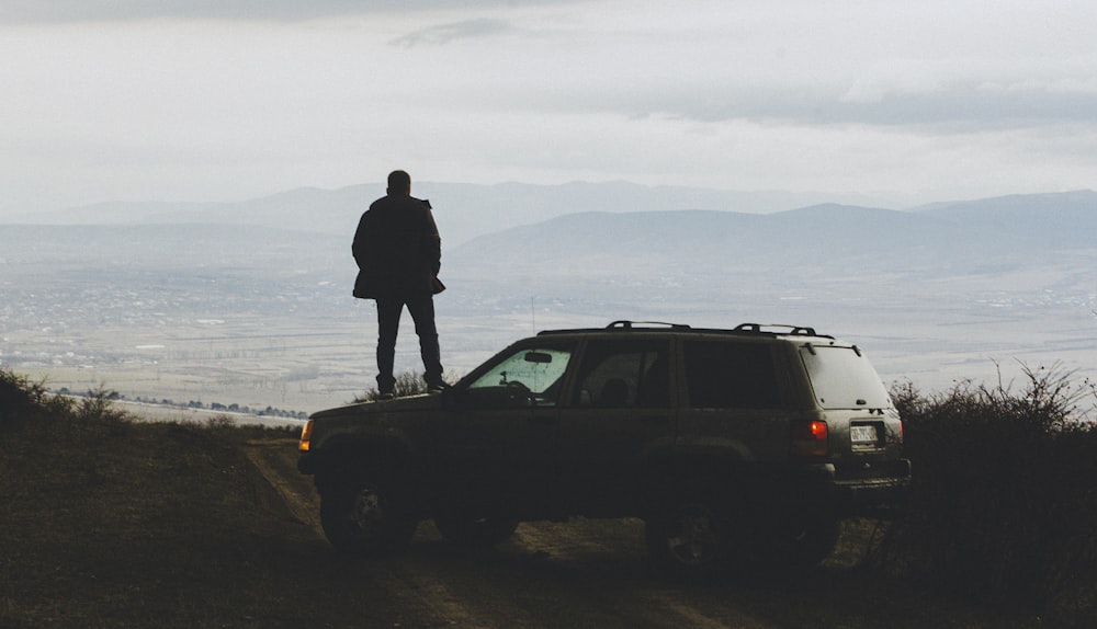 a man standing on top of a car on a dirt road