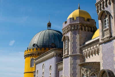 An ornate and colorful palace featuring a mix of architectural styles. Prominent features include a yellow, rounded tower with a dark dome and intricately patterned tile work in blue and white. The design incorporates elements of Romanticism with decorative masonry and arched windows.