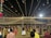 A nighttime gathering with numerous people dressed in traditional attire, dancing or socializing under a canopy of hanging lights. The event appears festive with the lights radiating a warm glow. Decorations can also be seen, including hanging colorful objects on the left side.