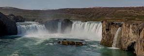 A wide shot of rolling hills with a waterfall cascading into a sparkling river below.