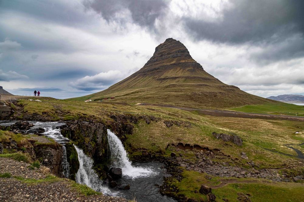 two people standing on a hill overlooking a waterfall