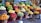 A vibrant and colorful display of various fruits arranged in wicker baskets. The assortment includes bananas, pineapples, oranges, grapes, apples, and other tropical and local fruits. The market setting adds a local and fresh vibe, with the fruits stacked neatly to create appealing patterns and textures.
