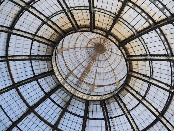 A large, intricate glass dome ceiling with a symmetrical pattern. The structure is made of metal frames and glass panels, radiating from the center.