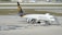 A UPS cargo airplane is parked on an airport tarmac with ground support equipment nearby. The plane is white with brown and gold detailing, featuring the logo and the words 'Worldwide Services' on its side. Several orange cones and cargo loading equipment are visible around the plane.
