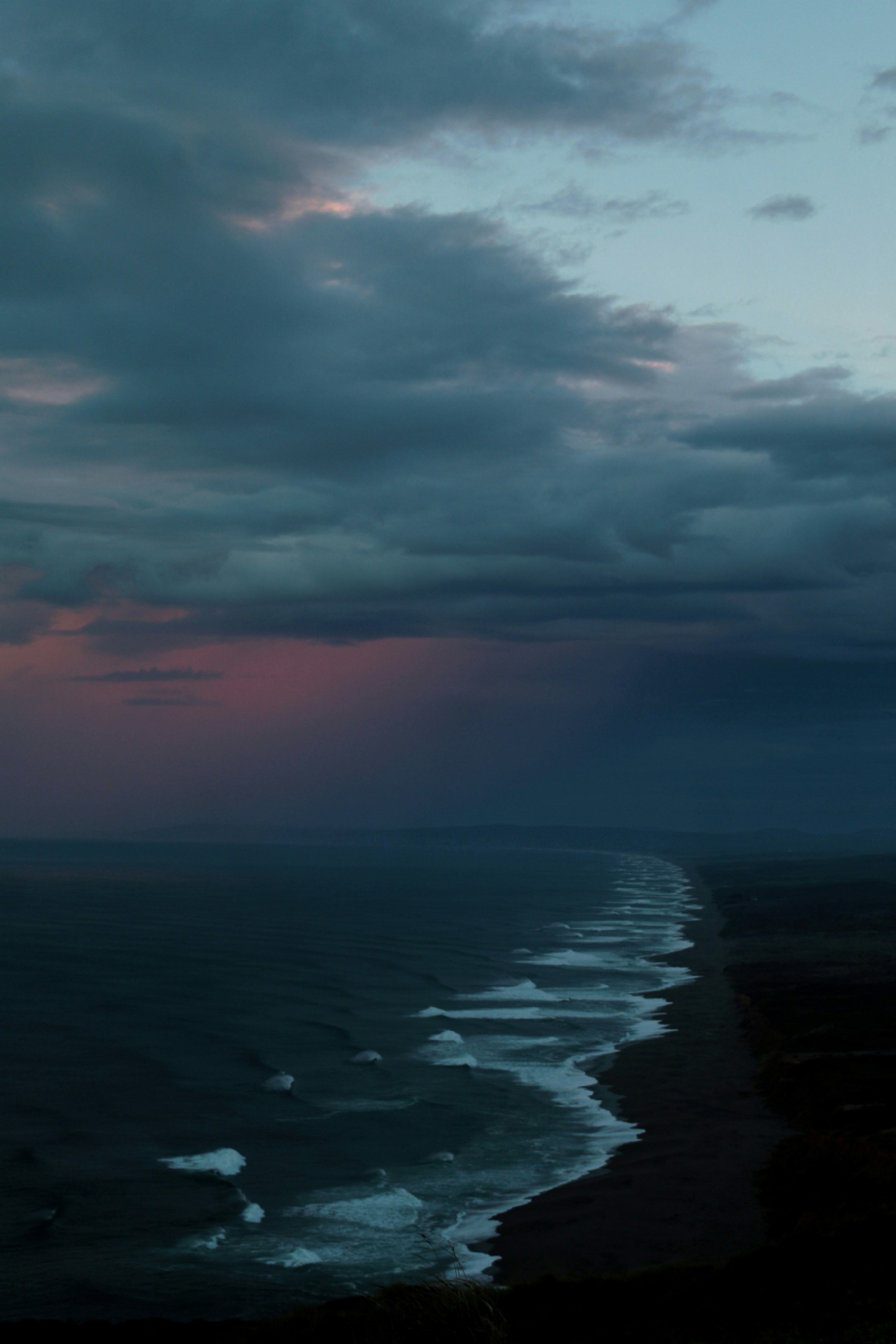 Dark ocean coastline with storm clouds and crashing waves at dusk