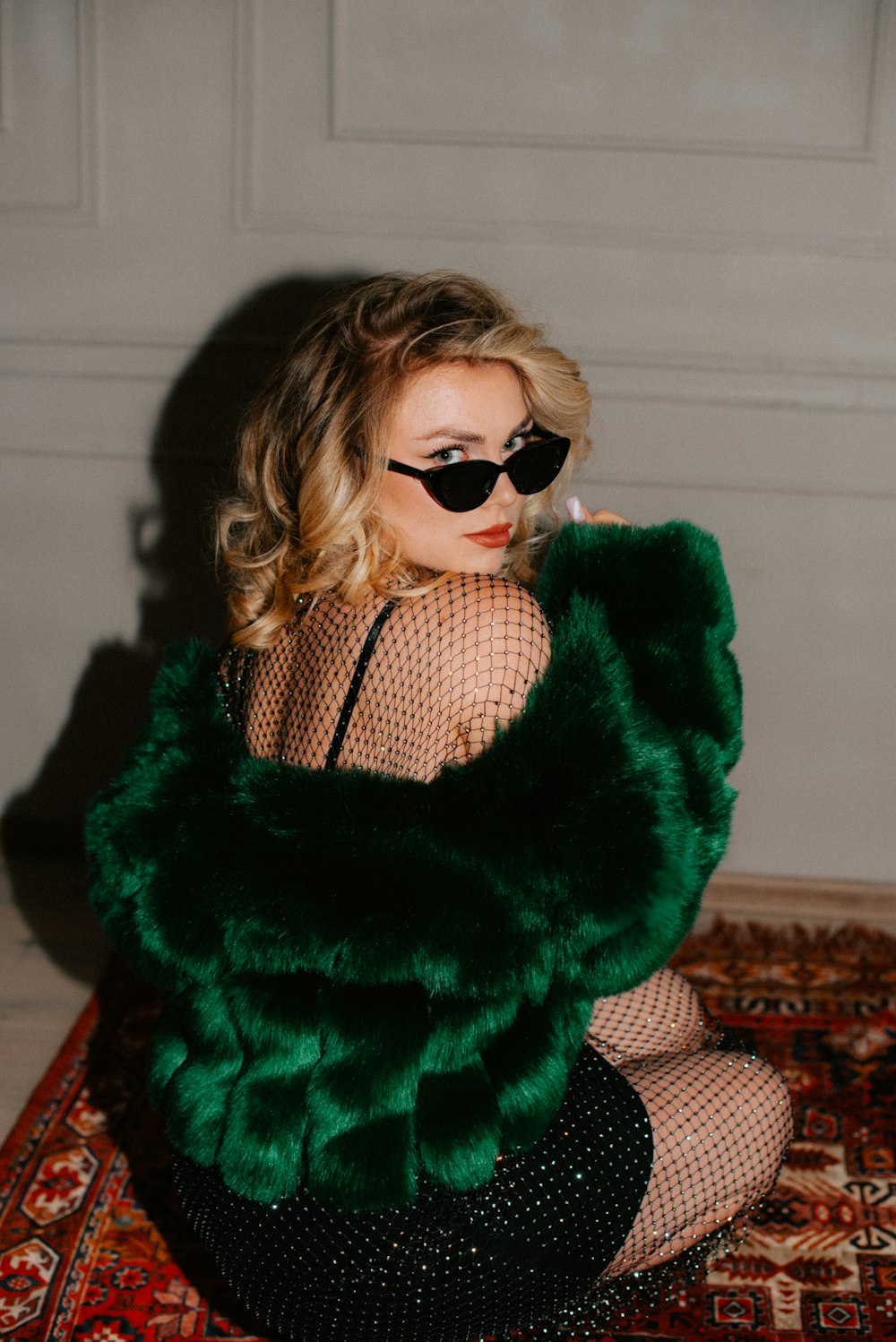 a woman sitting on a rug wearing a green fur coat