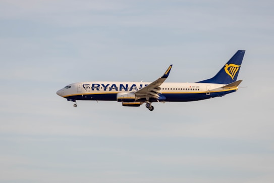A commercial airplane flies through a clear sky. The aircraft is painted in Ryanair's blue and white livery, with the company's logo prominently visible on the tail.