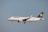 A Lufthansa passenger airplane is in flight, captured from a side view against a clear sky. The aircraft's landing gear is extended, and the Lufthansa logo is visible on the tail and fuselage.