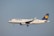 A Lufthansa passenger airplane is in flight, captured from a side view against a clear sky. The aircraft's landing gear is extended, and the Lufthansa logo is visible on the tail and fuselage.