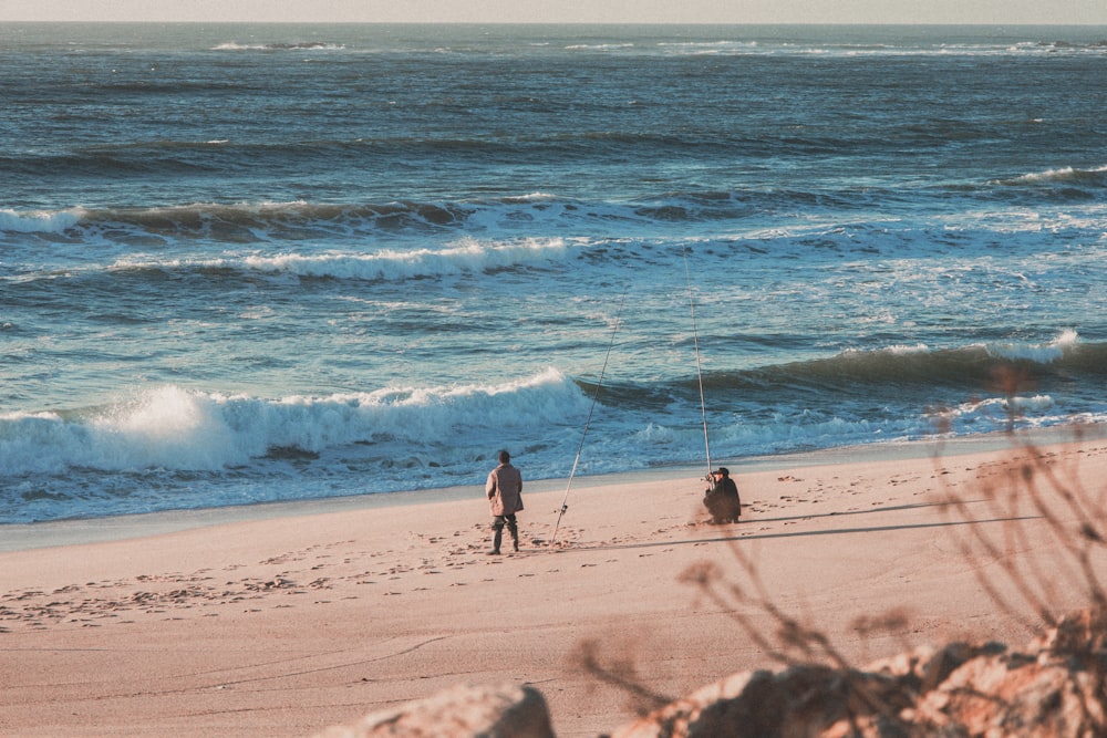 a couple of people standing on top of a sandy beach