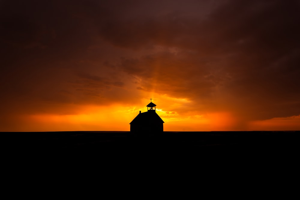 the sun is setting behind a barn in a field