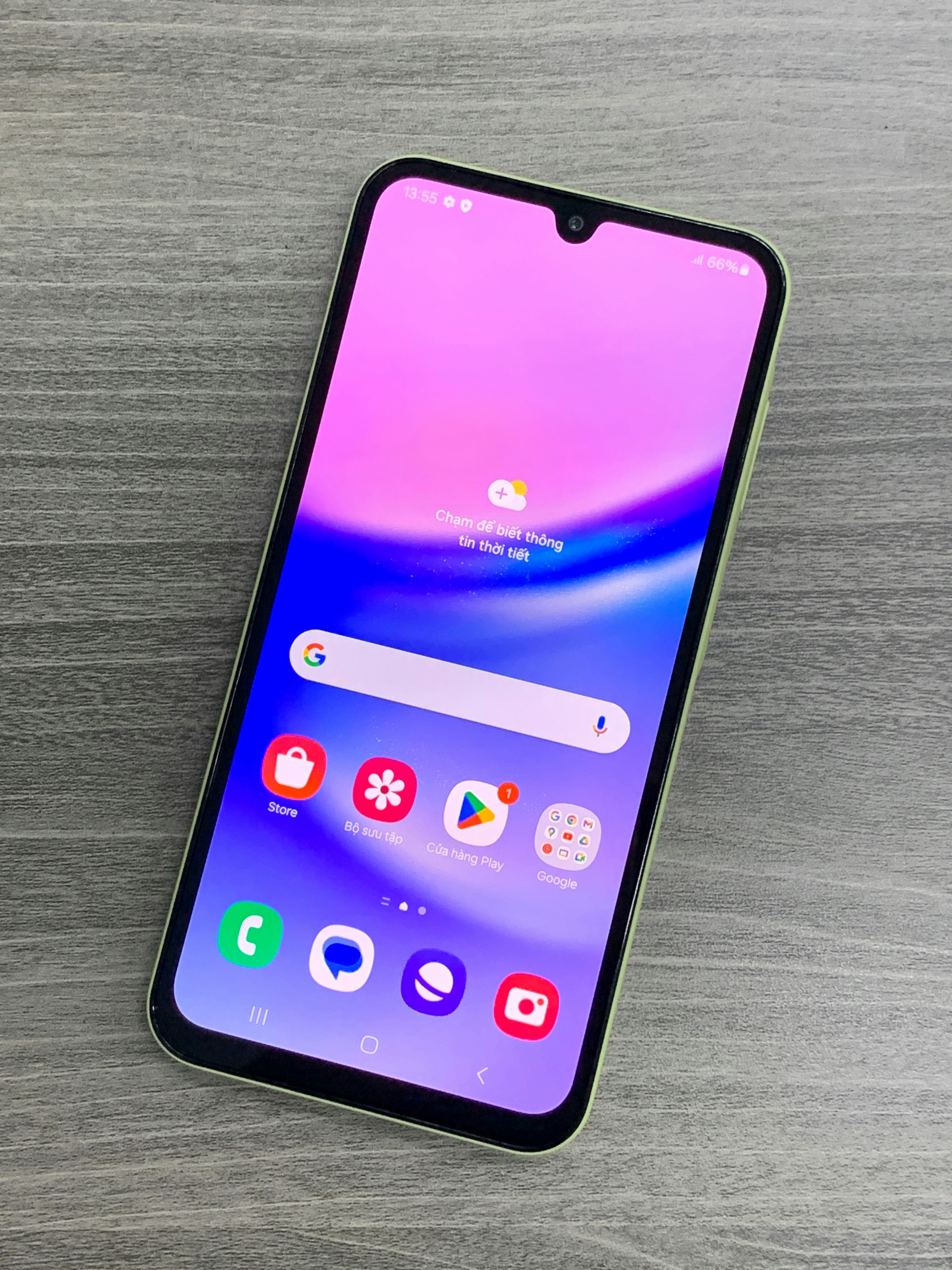 A smartphone with a colorful display featuring various app icons such as Store, Gallery, Google Play, and Google, is lying on a wooden surface. The screen has a gradient background of pink and purple shades.