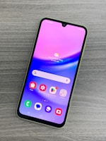 A smartphone with a colorful display featuring various app icons such as Store, Gallery, Google Play, and Google, is lying on a wooden surface. The screen has a gradient background of pink and purple shades.