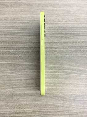 A green smartphone is placed flat on a textured surface, viewed from the side. The phone's buttons are visible, and the overall design is sleek and modern.