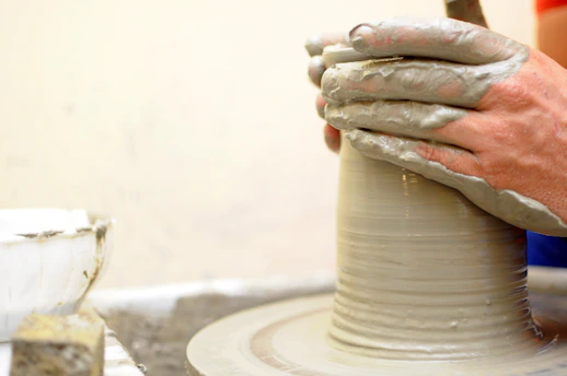Close-up of hands shaping wet clay on a pottery wheel, with earth-toned background.