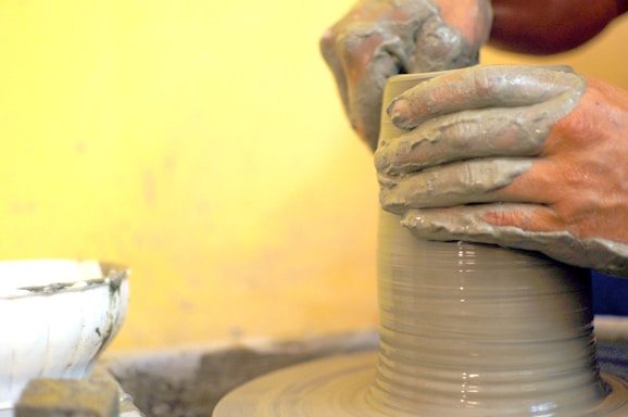 A cozy pottery studio corner with hands shaping a clay pot on the wheel, warm light casting gentle shadows.
