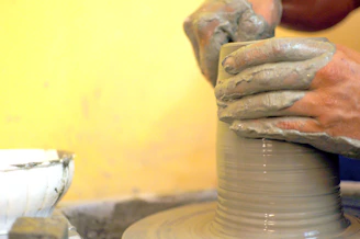 A joyful moment showing hands shaping clay on a potter’s wheel surrounded by colorful glazes.