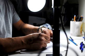 Close-up of hands drafting on a technical drawing table lit by a warm desk lamp.