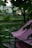 A pink tent is set up outdoors on a wooden platform surrounded by lush green foliage. Soft, ambient lighting is visible in the background, creating a serene atmosphere. The setting appears to be a garden or a park, with trees and plants adding to the natural scene.