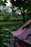 A pink tent is set up outdoors on a wooden platform surrounded by lush green foliage. Soft, ambient lighting is visible in the background, creating a serene atmosphere. The setting appears to be a garden or a park, with trees and plants adding to the natural scene.