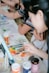 A group of people engaged in a painting activity, focusing on a table covered with various art materials. Paint tubes, brushes, and a colorful palette are prominently displayed, suggesting a creative and collaborative environment.