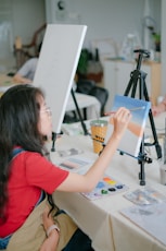 a young girl painting on a canvas at a table