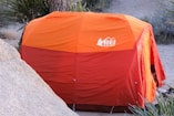 an orange and red tent sitting on top of a rock