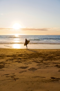 A friendly surfer holding a surfboard near the ocean at sunset.
