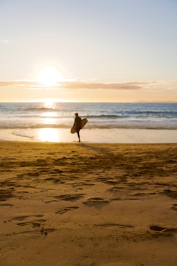 A friendly surfer holding a surfboard near the ocean at sunset.