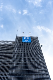 A multi-story parking structure with metal grid facade rising towards a bright sky. A blue sign labeled 'P2' is prominently displayed on the building, indicating a parking level.
