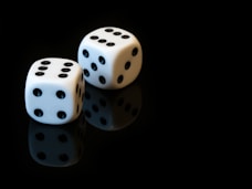 two white dices sitting on top of a black surface