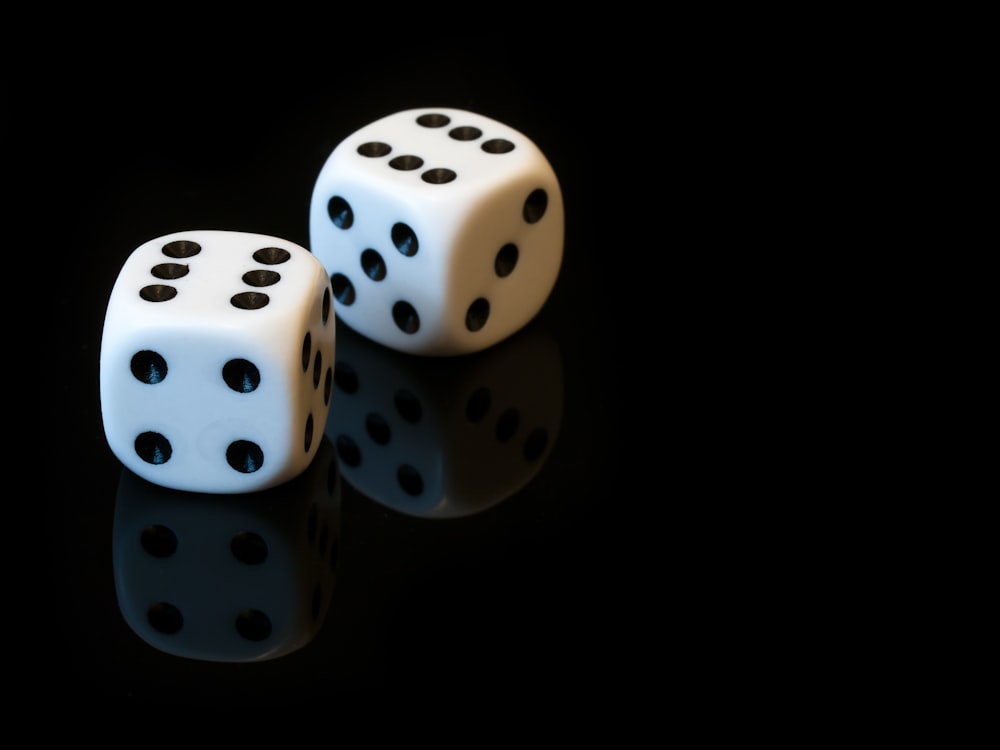two white dices sitting on top of a black surface