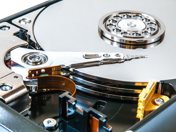 An open hard drive is displayed, showcasing the shiny metallic disk platters, the spinning spindle, and the read/write actuator arm. The intricate components are visible, highlighting the precision engineering involved in its design.
