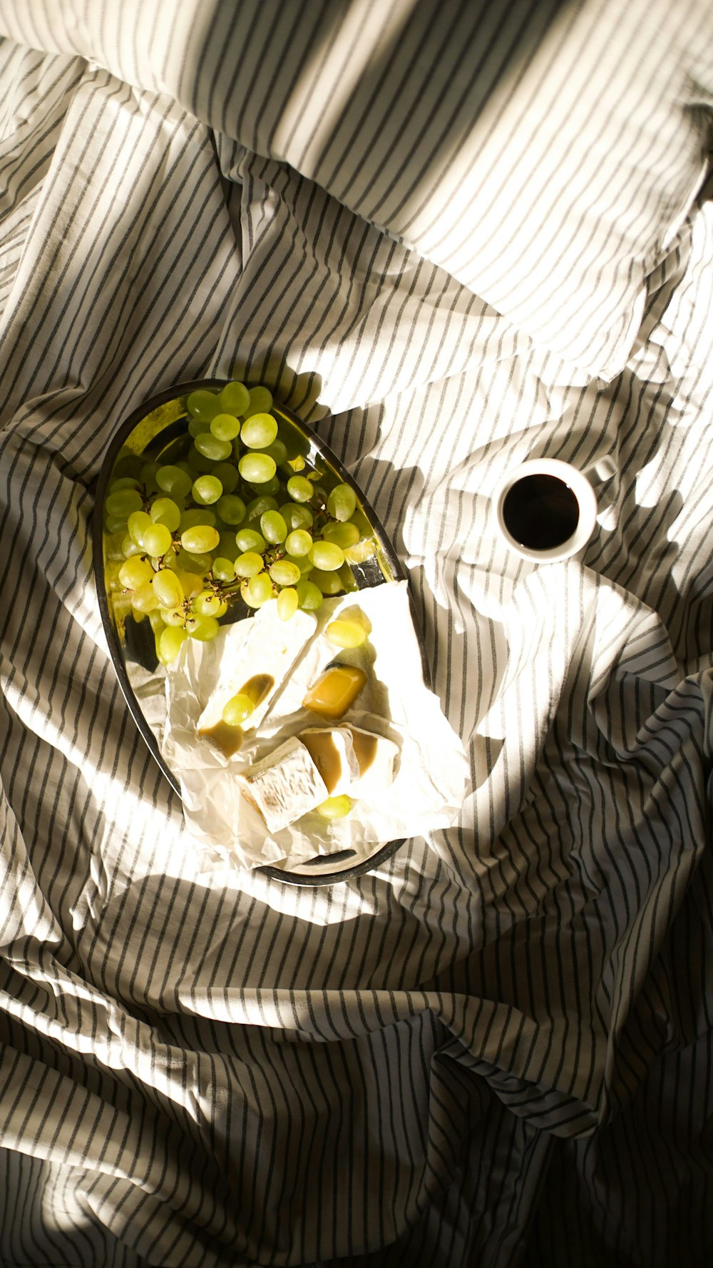 un cuenco de uvas y una taza de café en una cama