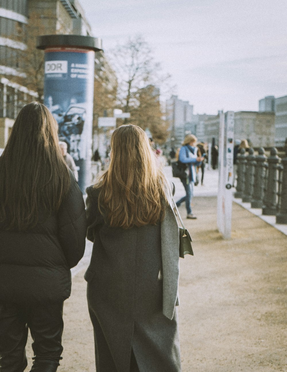 two women walking down a sidewalk next to a fence