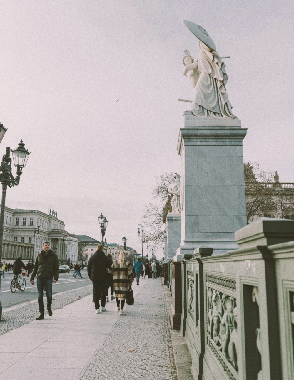 a group of people walking down a sidewalk next to a statue