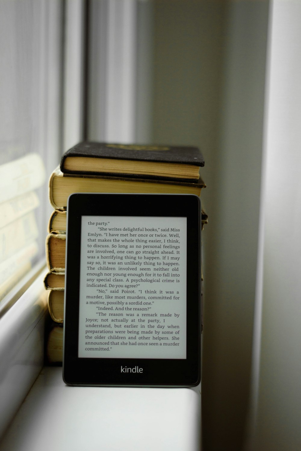 a kindle sitting on a window sill next to a stack of books