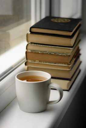 A cozy workspace with stacks of vintage engineering books and a steaming cup of tea by a window.