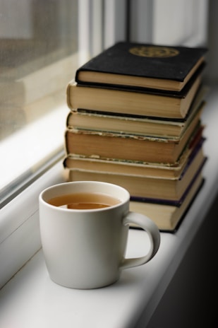 A stack of comforting books arranged next to a steaming cup of tea.