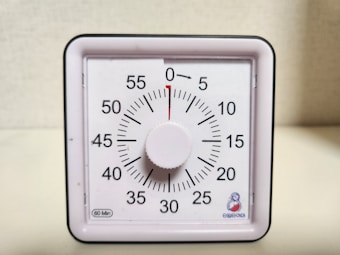 A square analog timer with a white face, black numbers, and a central knob. The timer is marked with numbers at five-minute intervals, and a red indicator shows the time set to 30 minutes.