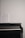 A black piano with a sheet of music placed on its open cover against a plain white wall.