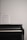 A black piano with a sheet of music placed on its open cover against a plain white wall.
