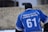 A person is seen from behind wearing a blue sports jersey with the text 'Himalayan Hawks Drass' and the number 61. The person is also wearing a black beanie. The background appears to be an outdoor setting.