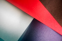 An arrangement of textured papers in various shades, overlapping each other at different angles. The colors include red, brown, purple, and light blue, creating a visually appealing contrast with the rough texture of the paper surfaces.